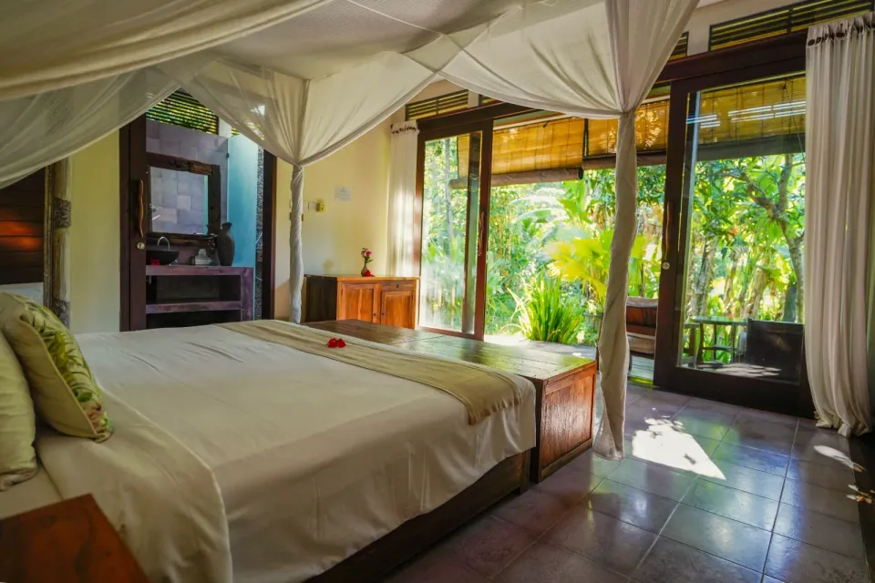 A canopy bed facing open doors and tropical greenery